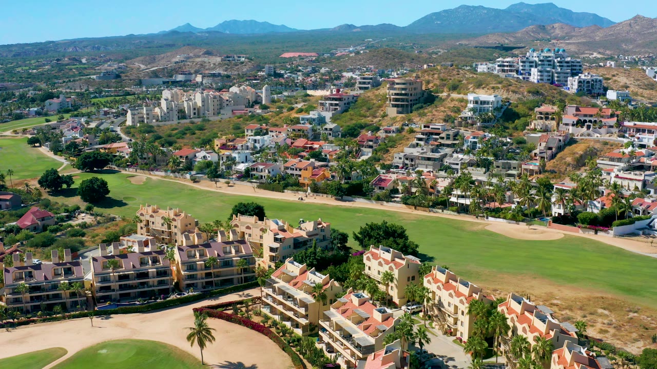 Drone view across a golf course with residential buildings and hills beyond