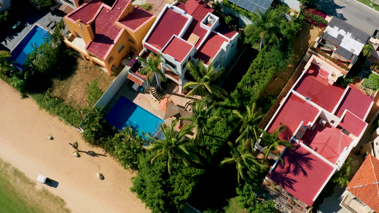 Closer overhead view of villas, red tile roofs, pools, palms, and solar panels.
