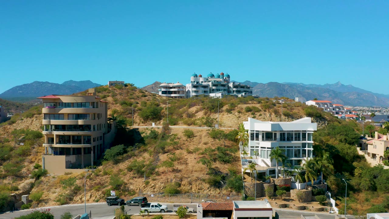 Residential hillside with modern buildings and clear blue sky.