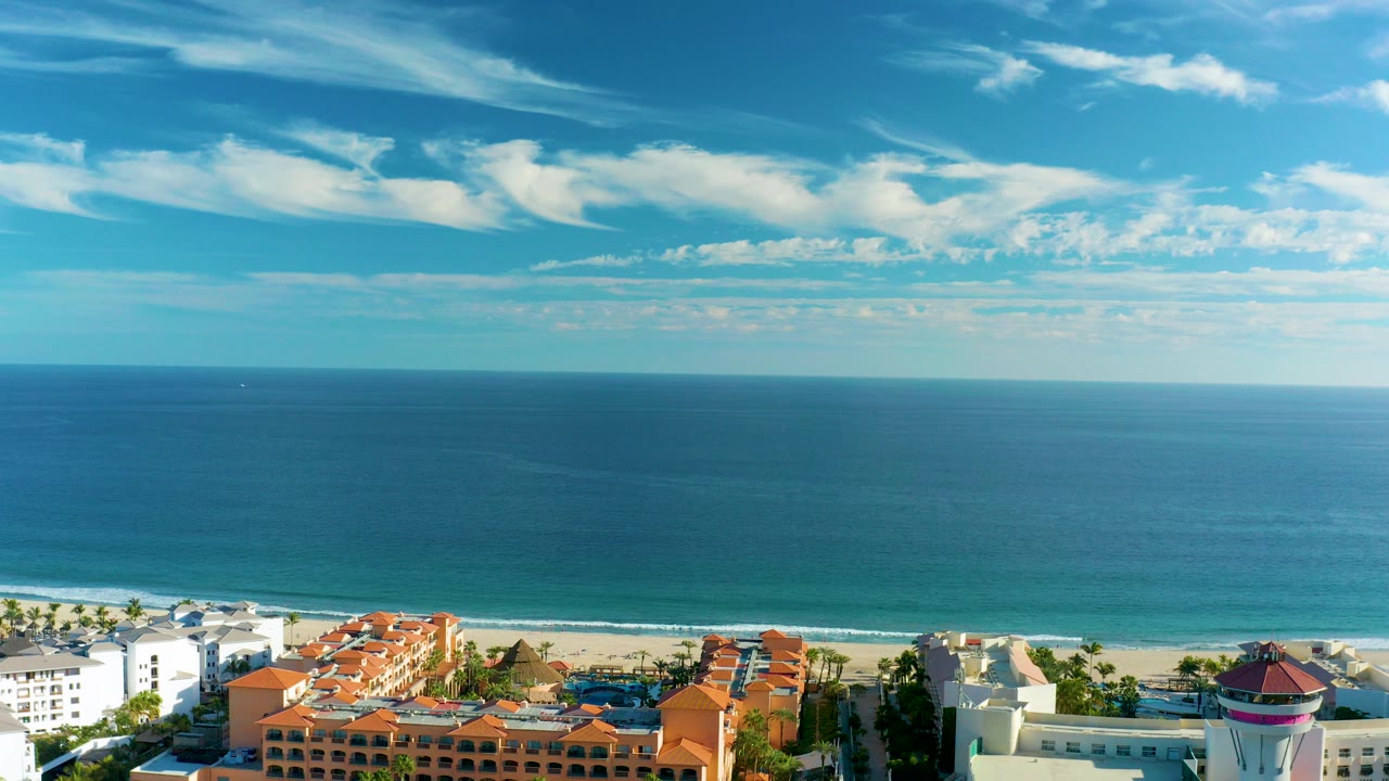 Aerial view of blue ocean, sandy beach, and coastal buildings.