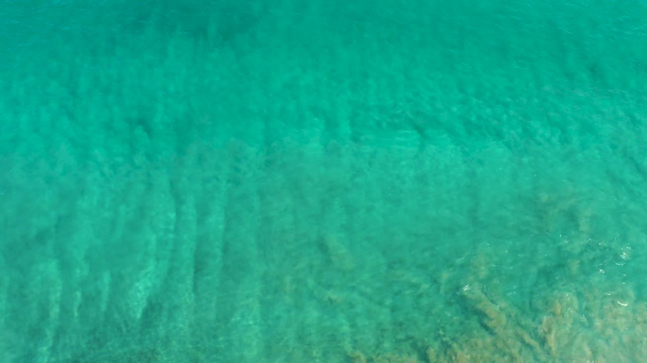 A slightly brighter patch of sandy bottom appears beneath turquoise San Jose Del Cabo water, with moving light streaks and no visible people.