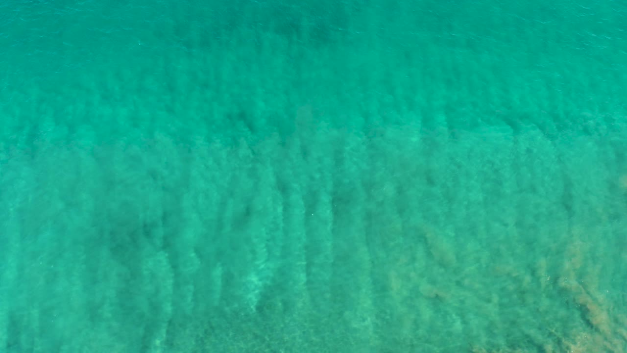 Transparent turquoise water covers a pale sandy seabed in San Jose Del Cabo, with faint darker streaks from ripple shadows and no visible people.