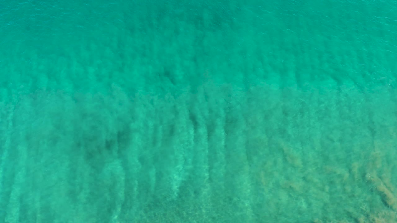 Shallow turquoise ocean water in San Jose Del Cabo fills the frame, with vertical light streaks and sandy bottom detail visible beneath the surface, and no visible people.