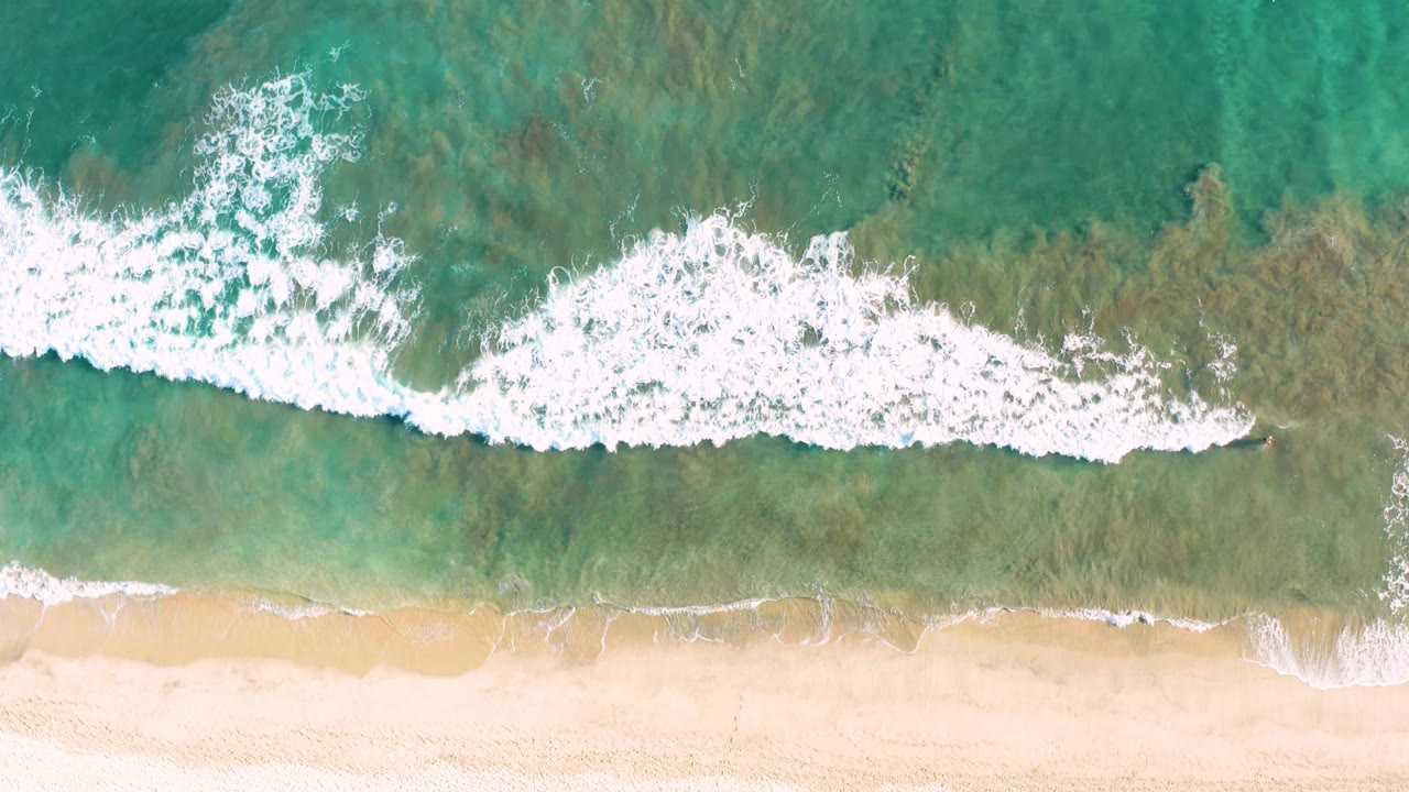 White foam spreads across green water near sand.