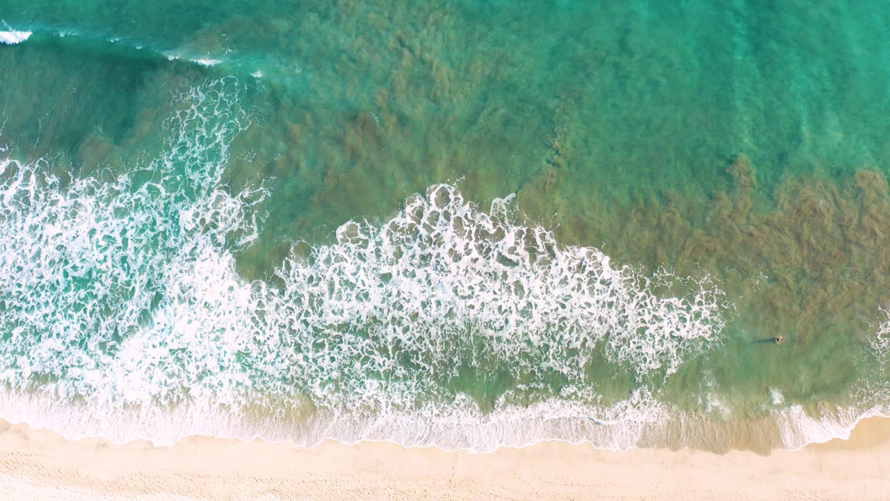 Overhead turquoise surf breaking onto a sandy beach.