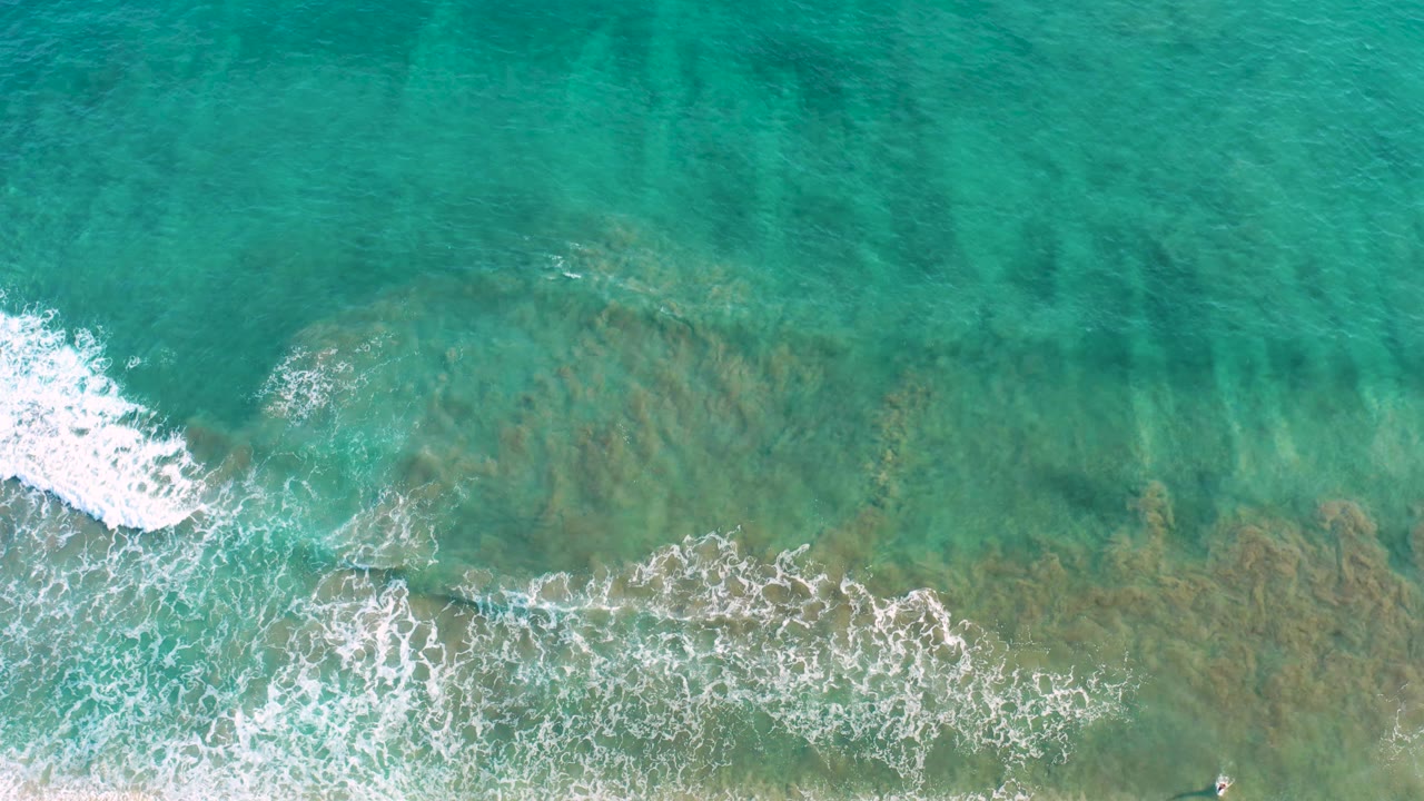 A foamy wave line advances across clear turquoise water in San Jose Del Cabo, Mexico, with the seabed visible beneath and no visible people.