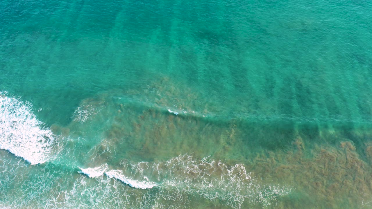 A low band of white surf crosses green-blue shallow water in San Jose Del Cabo, Mexico, with underwater texture visible and no visible people.