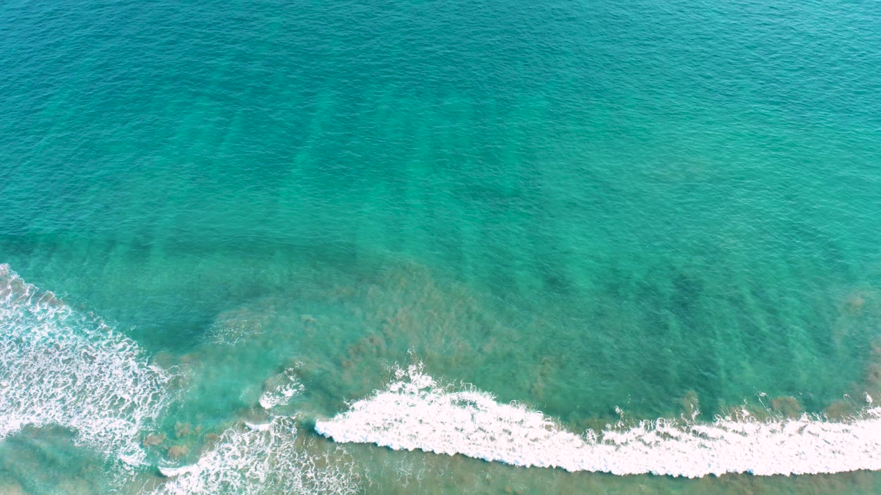 Turquoise ocean surface with white foam entering from the lower edge.