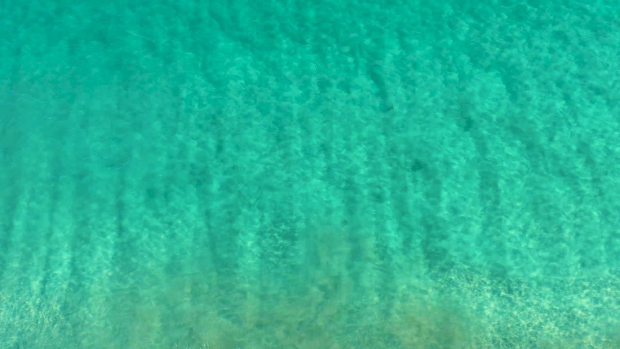 Straight-down view of clear turquoise ocean water over a sandy seabed in San Jose Del Cabo, with fine surface ripples and no visible people.