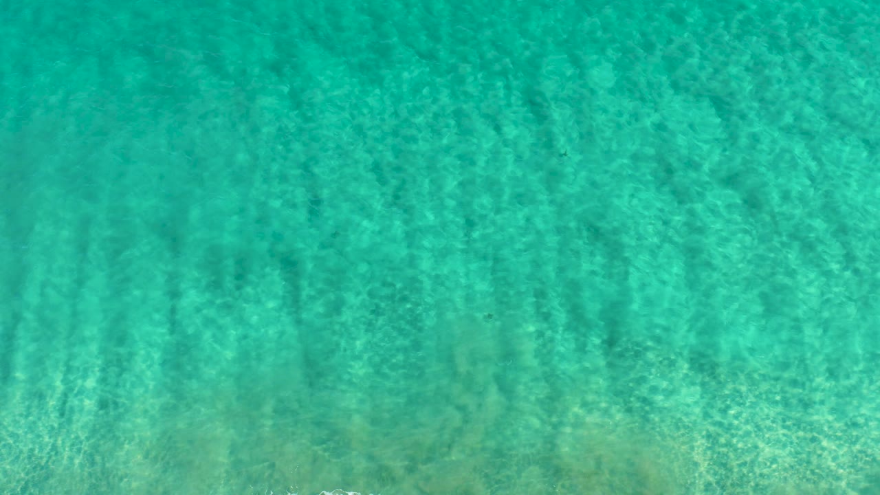 Transparent turquoise water in San Jose Del Cabo shows darker vertical seabed streaks under soft ripples, with no visible people.