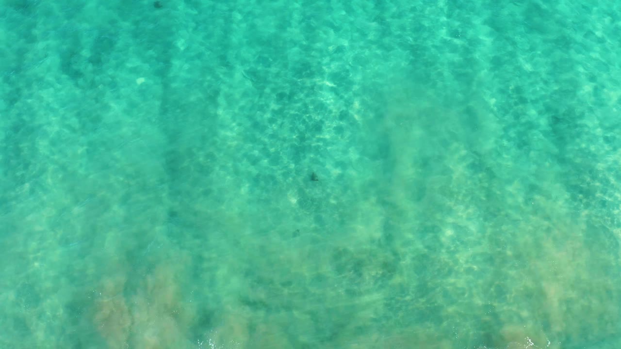 Top-down view of turquoise water over a sandy seabed in San Jose Del Cabo, with faint ripple lines and no visible people.