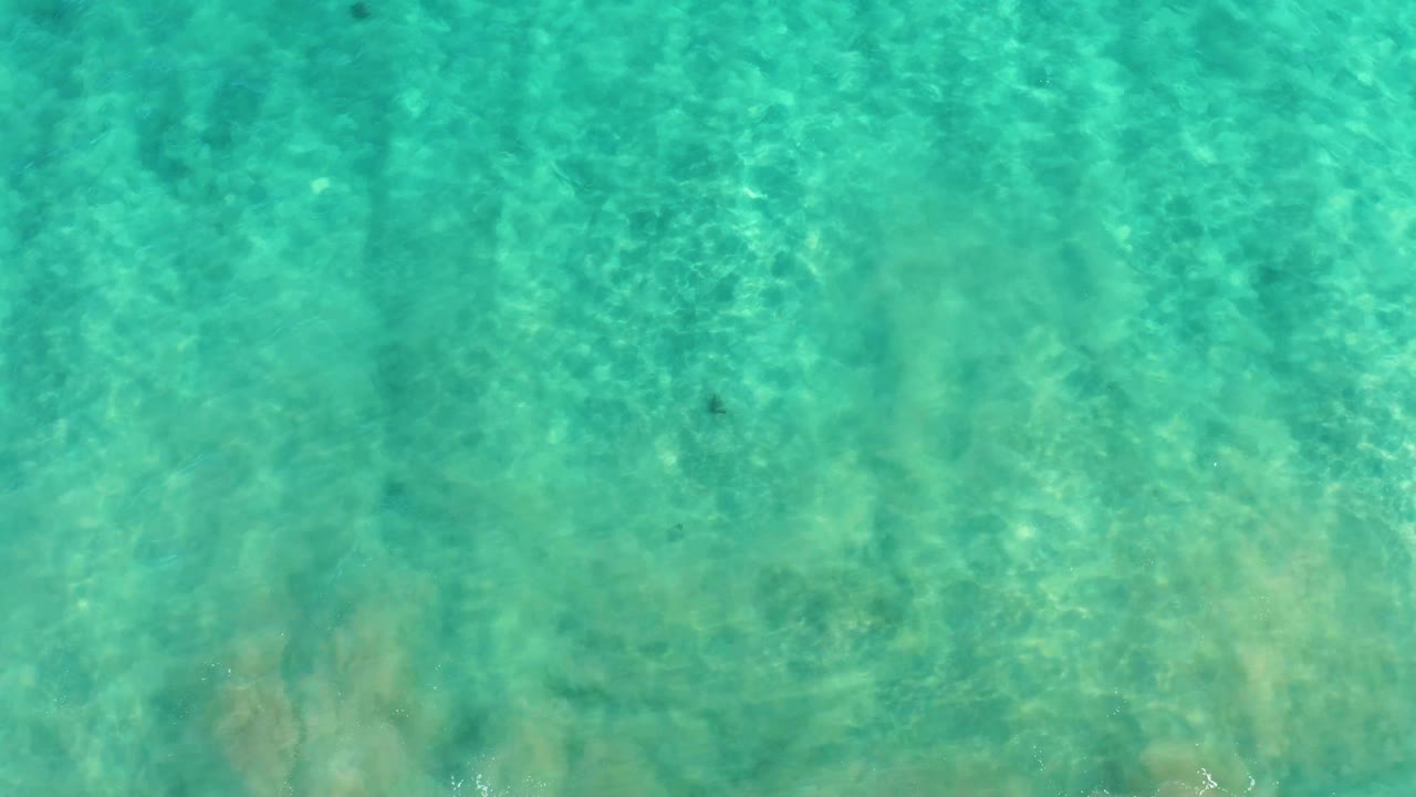 Clear turquoise ocean water in San Jose Del Cabo fills the frame, with subtle surface movement shifting light across the sand and no visible people.