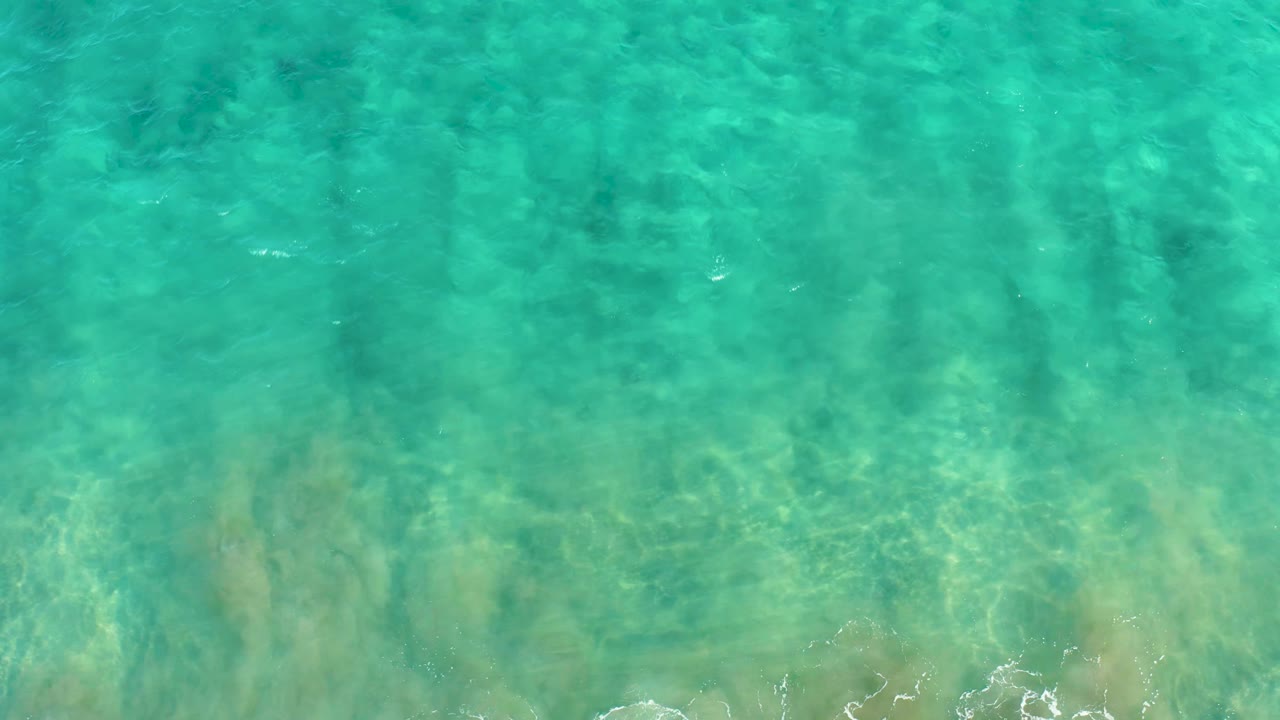 Clear blue-green water in San Jose Del Cabo shows rippled light over the sandy bottom, with a small foam edge near the lower frame and no visible people.