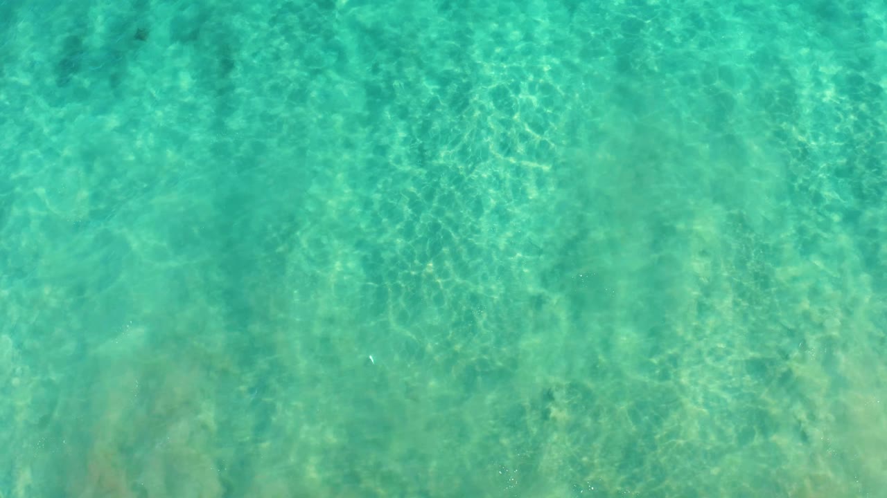 Clear teal ocean water covers a sandy seabed in San Jose del Cabo, with faint darker patches and no visible people.