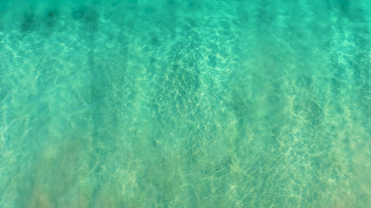 Transparent green-blue water in San Jose del Cabo includes a small white wave line near the upper right and no visible people.