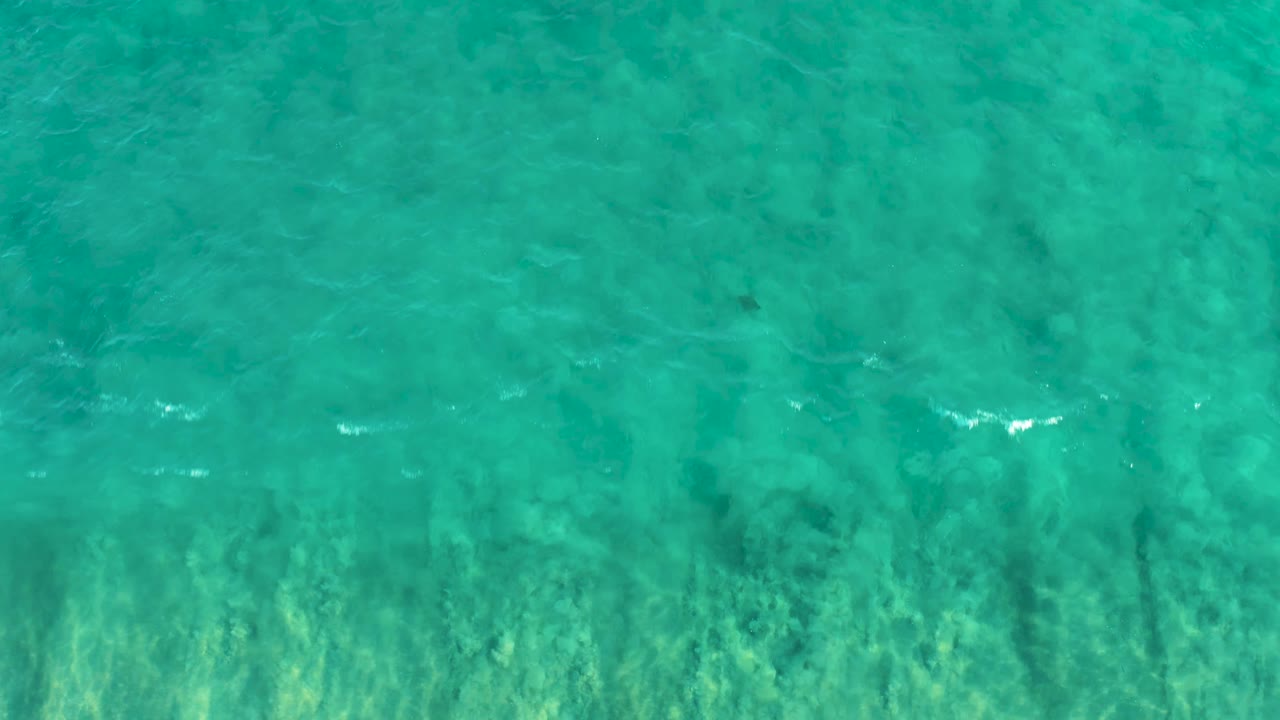 Clear blue-green ocean water in San Jose Del Cabo, with small white foam marks appearing near the lower edge and no visible people.