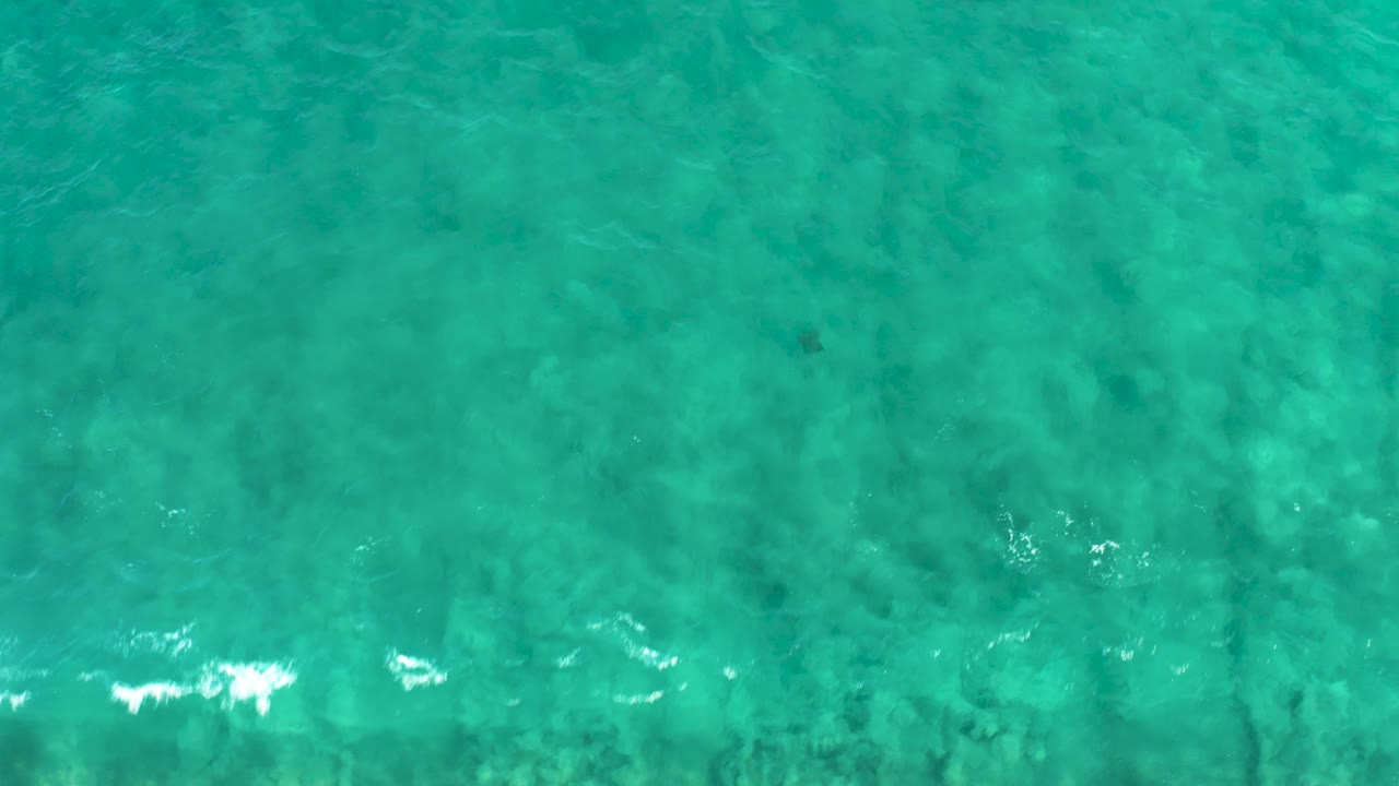 Turquoise ocean water in San Jose Del Cabo with a brighter foam streak crossing the lower area, darker seabed patches, and no visible people.
