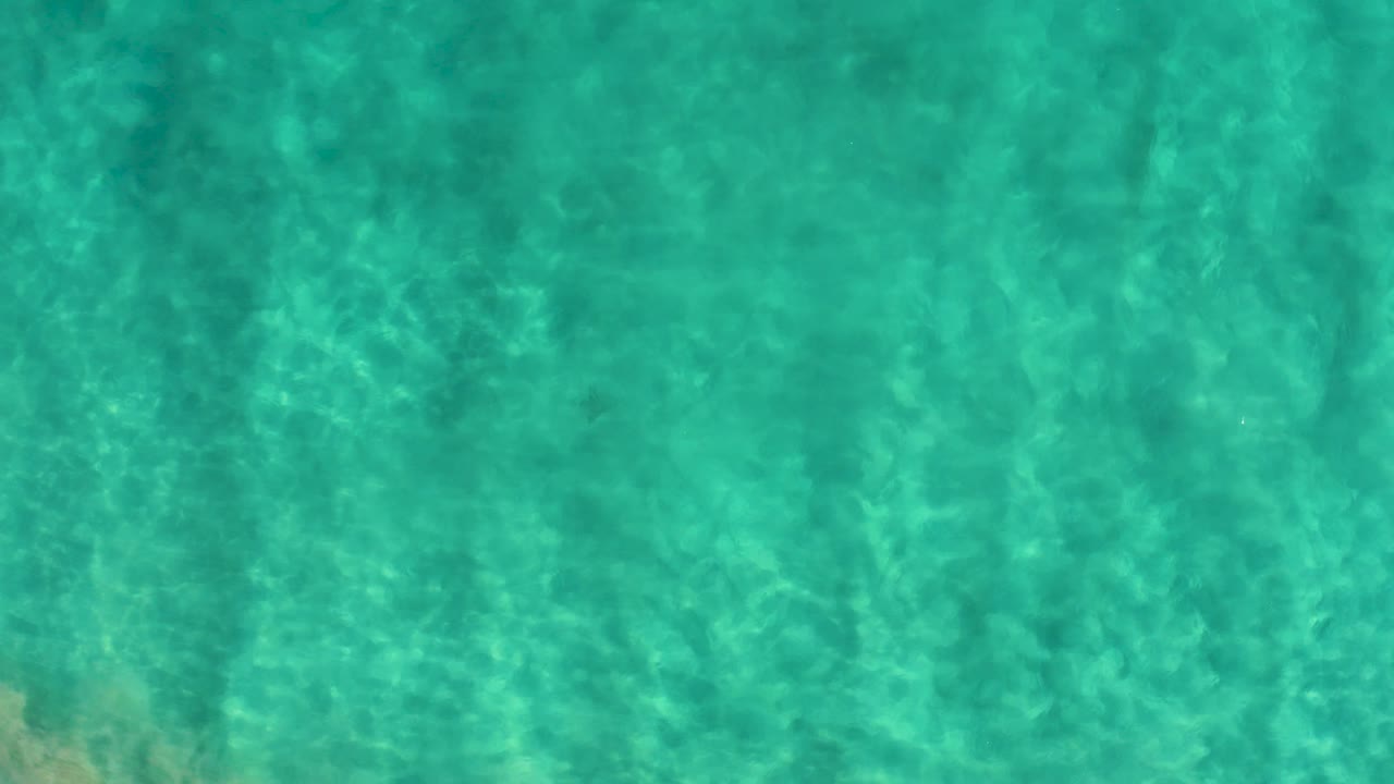 Turquoise shallow ocean water in San Jose Del Cabo, Mexico, with bright ripple highlights and darker submerged patches on the seabed, no visible people.