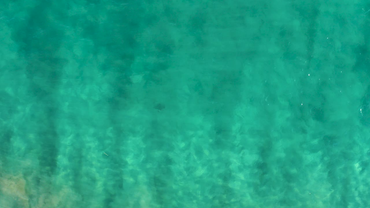 Top-down view of clear turquoise water in San Jose Del Cabo with muted sandy seabed patterns and no visible people.