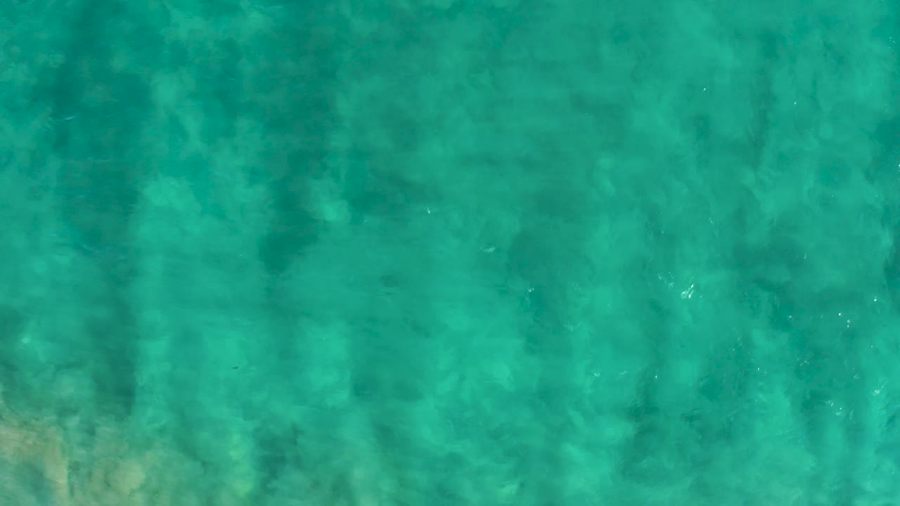 A straight-down frame of turquoise San Jose Del Cabo water shows faint darker underwater shadows and no visible people.