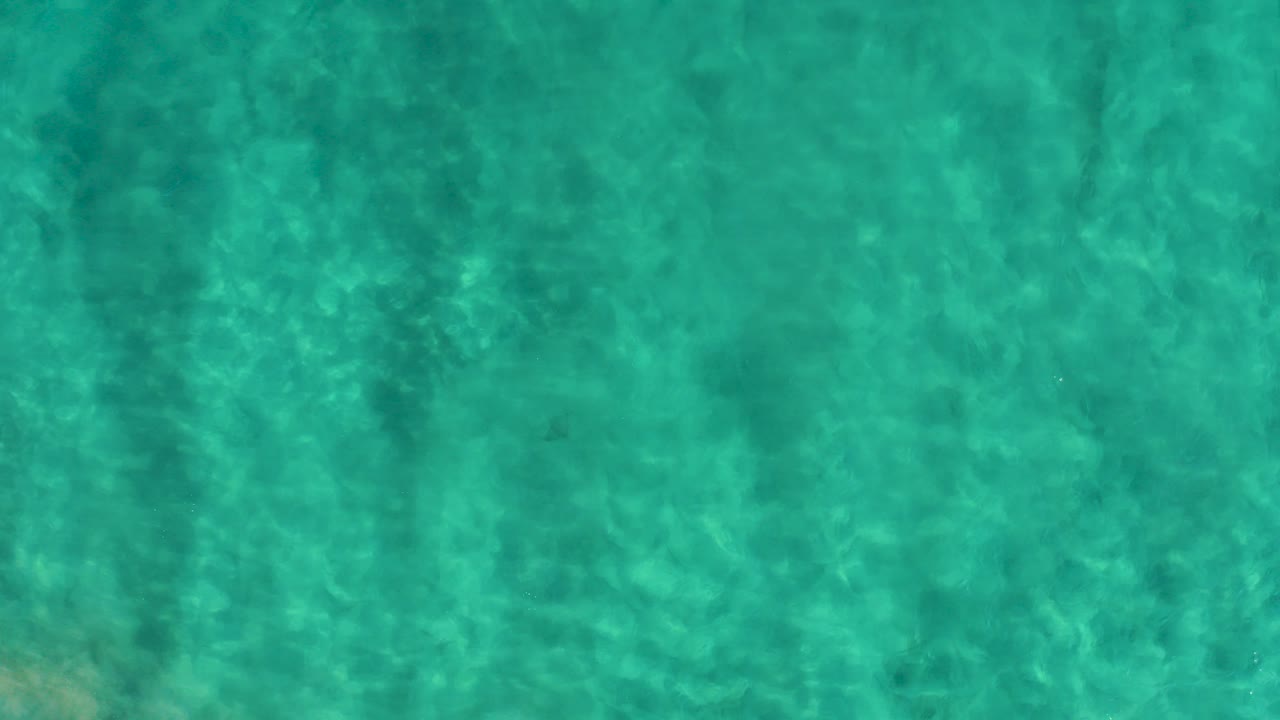 Clear turquoise shallow water in San Jose del Cabo with faint bottom texture, darker wavy shadows near the left side, and no visible people.