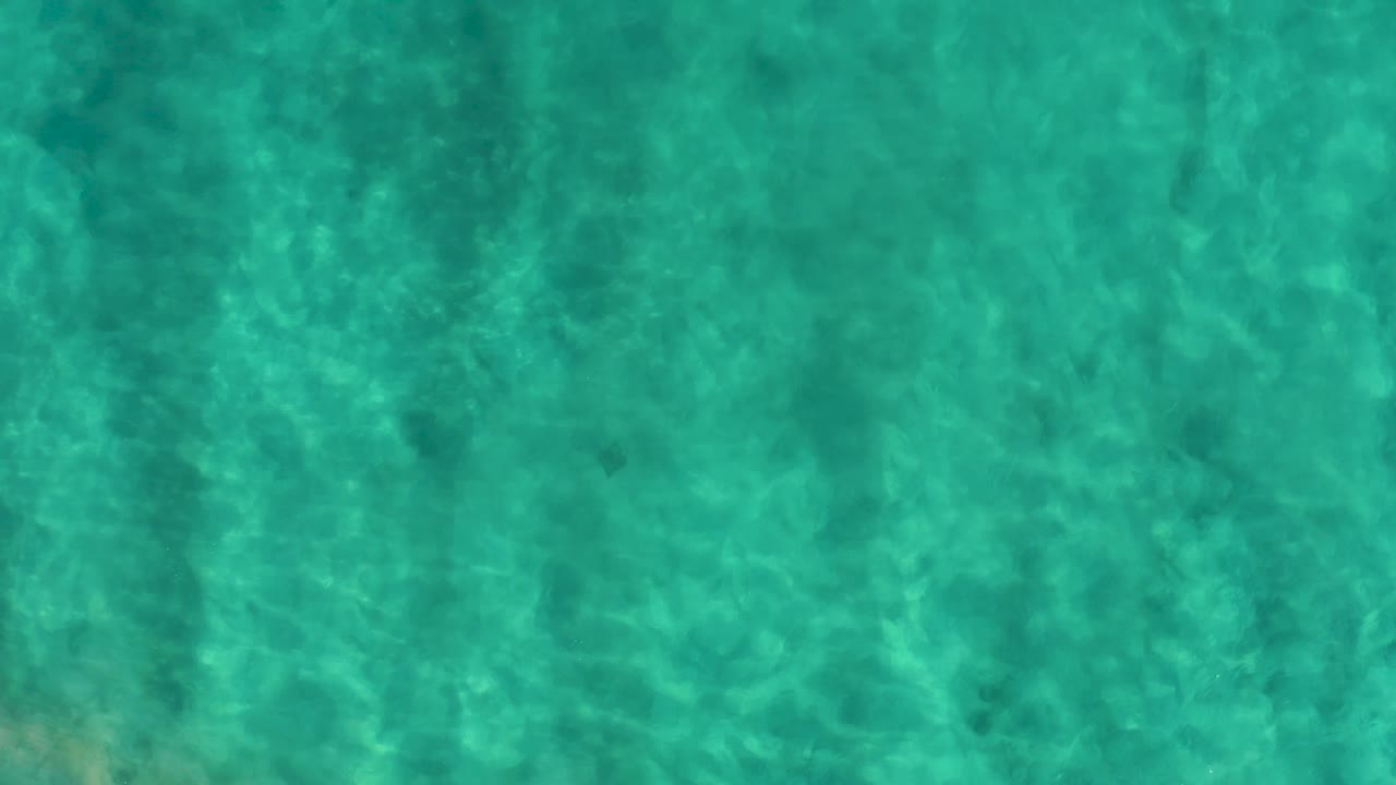 Blue-green shallow water in San Jose del Cabo shows a slightly darker band of underwater shadow across the frame and no visible people.