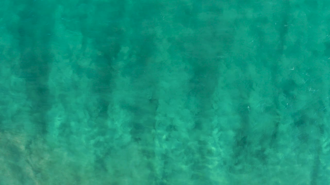 Turquoise ocean water with faint vertical shadows over a sandy bottom