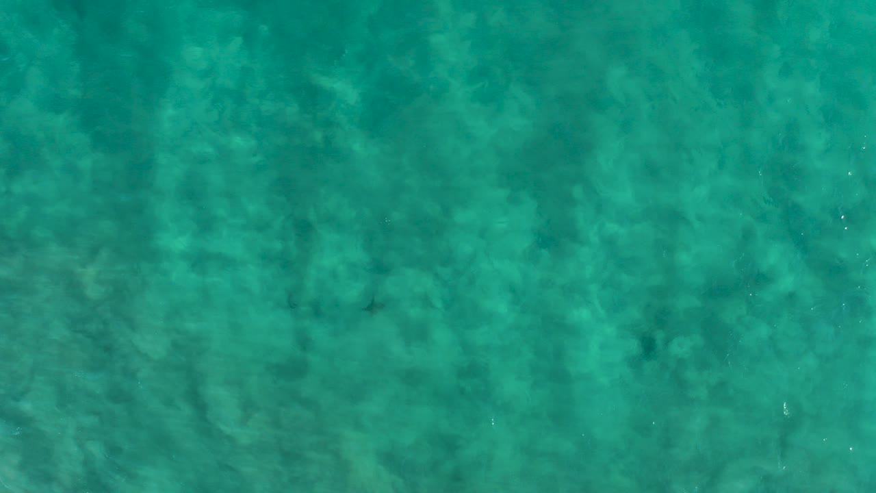 Overhead view of clear turquoise ocean water in San Jose del Cabo with faint sandy seabed textures and no visible people.