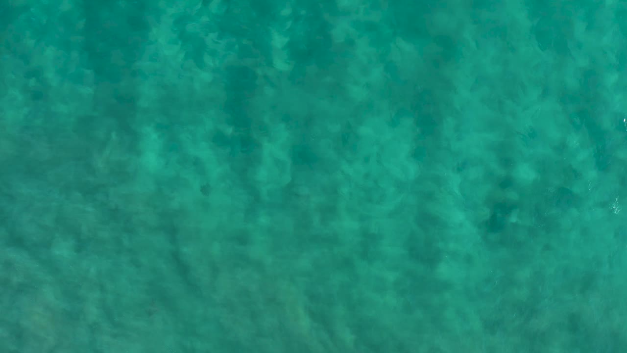 Blue green shallow water in San Jose Del Cabo fills the frame, with darker seabed patches shifted slightly by surface movement and no visible people.