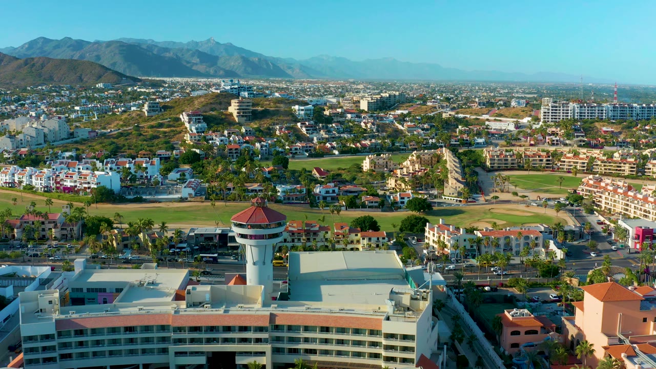 Drone view over water tower, roads, houses, fields, and mountain horizon.