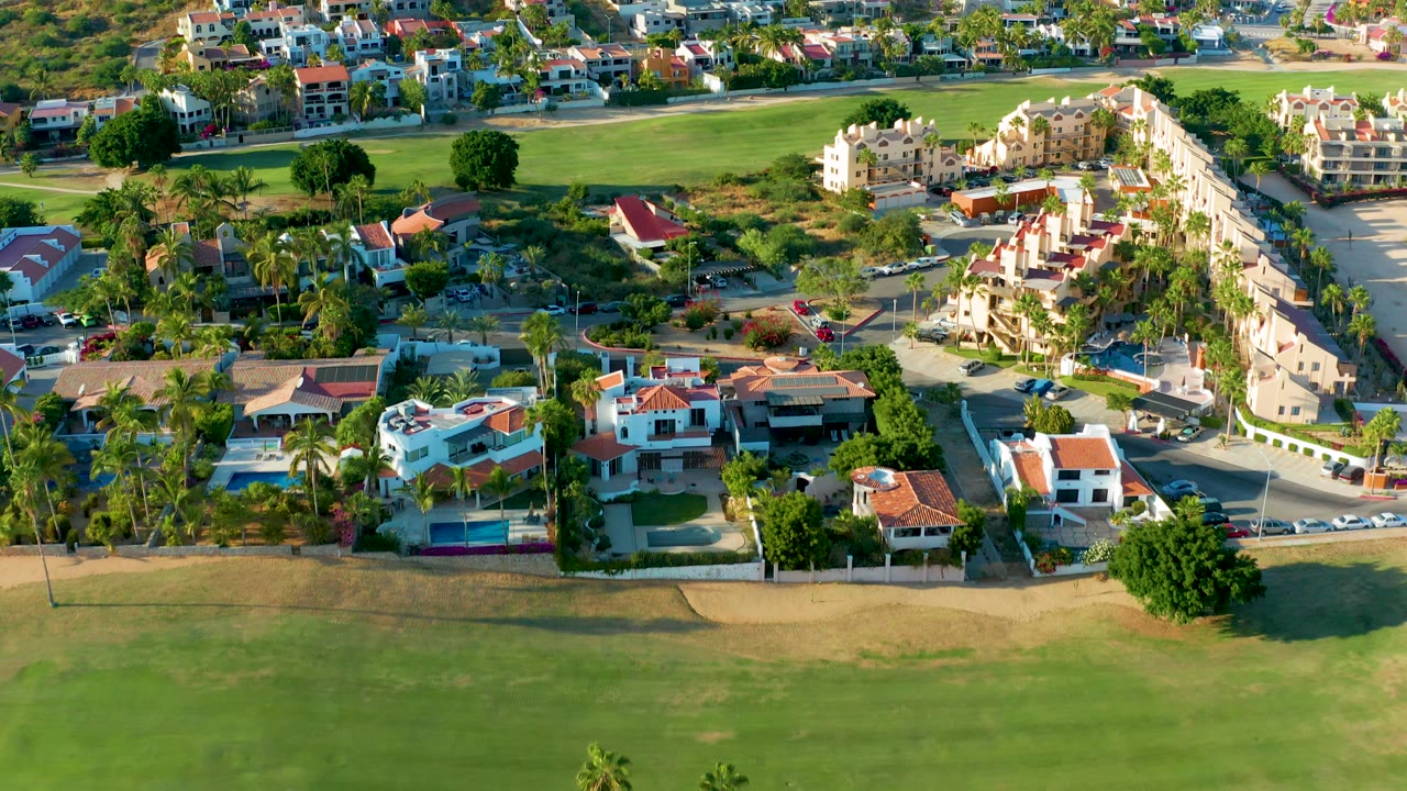 Drone view of homes, palm trees, and golf course grass in warm sunlight.