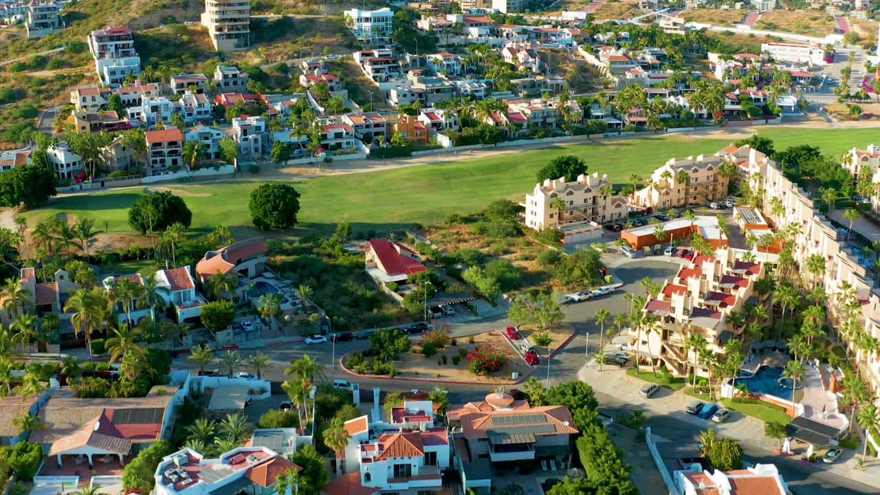Residential blocks, palm trees, roads, and a large green field from above.