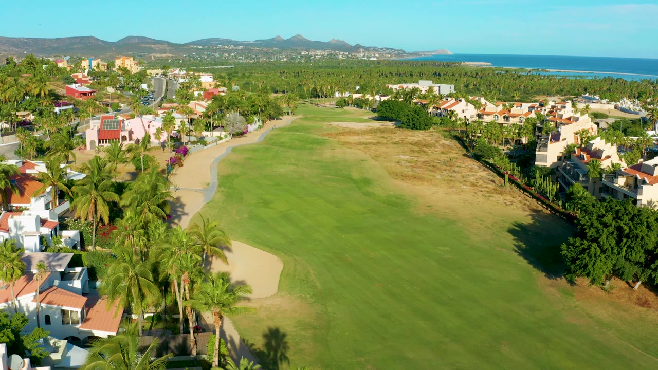 Golf fairway with palms, houses, mountains, and ocean beyond.