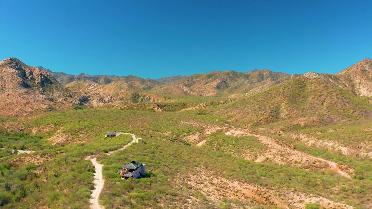 Wide aerial landscape with SUV on dirt road below mountains
