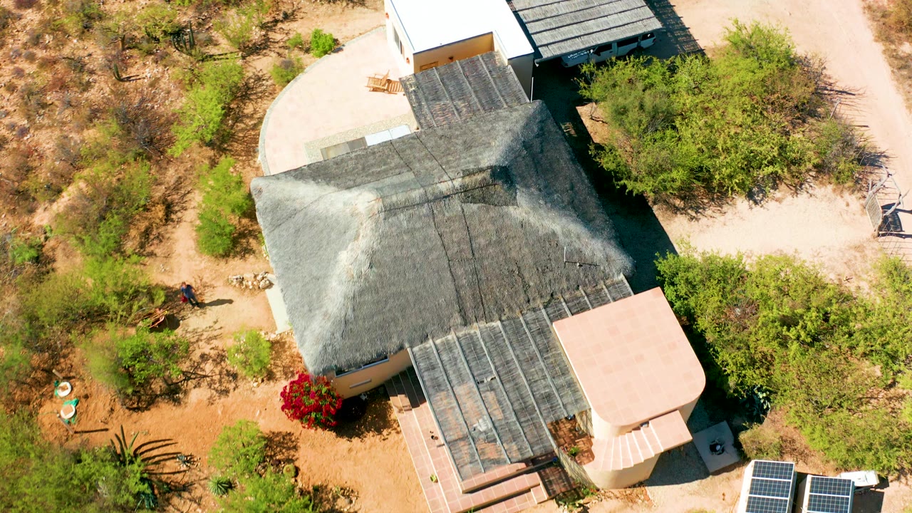 Top-down frame of the Cabo Pulmo residence as the white adjoining structure and dark shade beside the roof become more prominent, with solar panels still visible and no visible people.