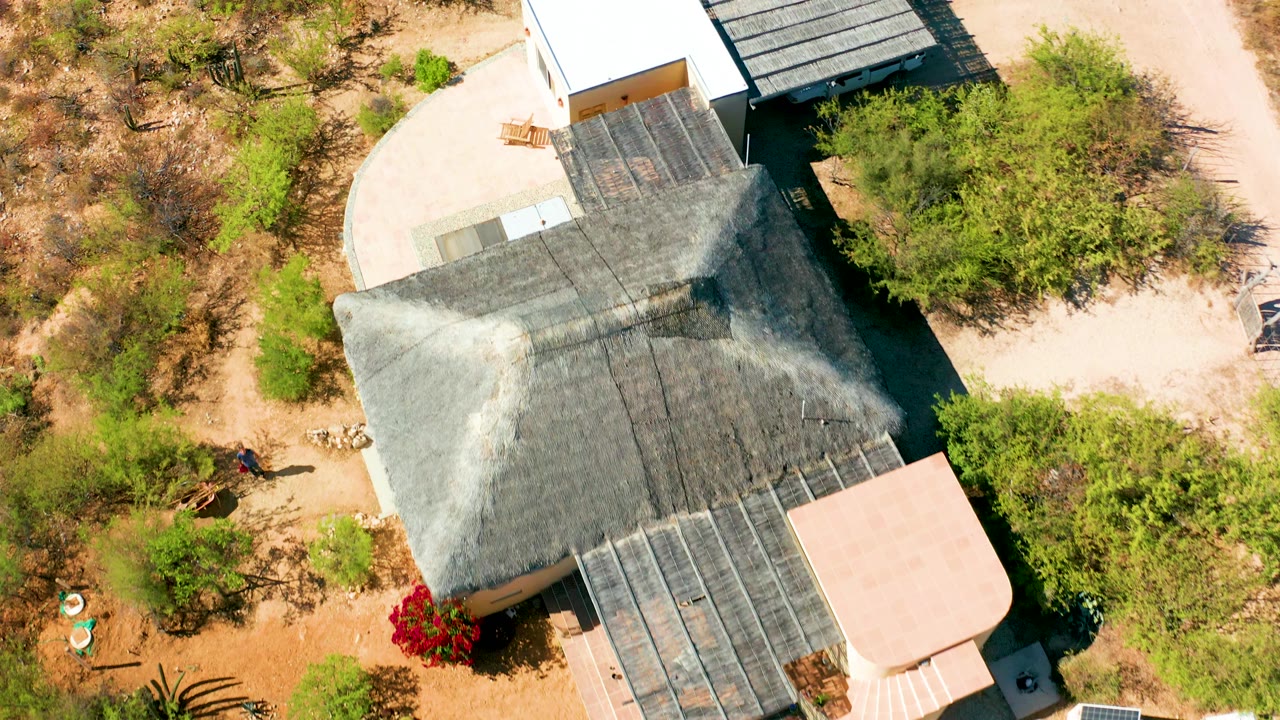 Overhead shot of a desert house with a large thatched roof and sparse vegetation.