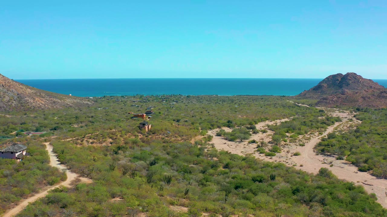 Aerial view of a vehicle on a dirt road through coastal scrub with hills and ocean beyond.