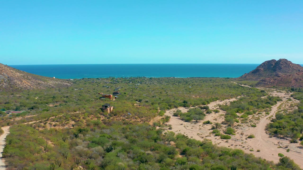 Elevated view over desert scrub and dirt roads toward a hill and ocean horizon.