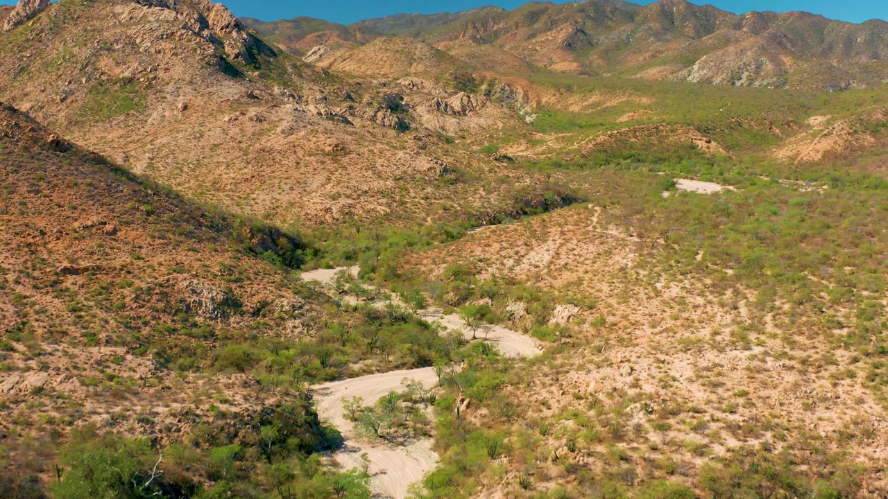 Aerial view of a dry desert wash below rocky hills.