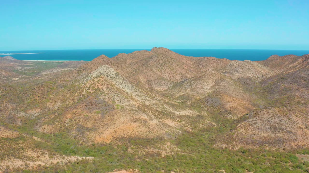 Wide elevated view over rocky Cabo Pulmo mountain ridges with sparse green vegetation, a blue ocean horizon, clear sky, and no visible people.
