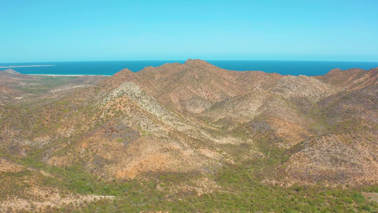 Cabo Pulmo mountain slopes fill the frame with mottled brown rock and low vegetation, backed by a level blue ocean horizon and no visible people.