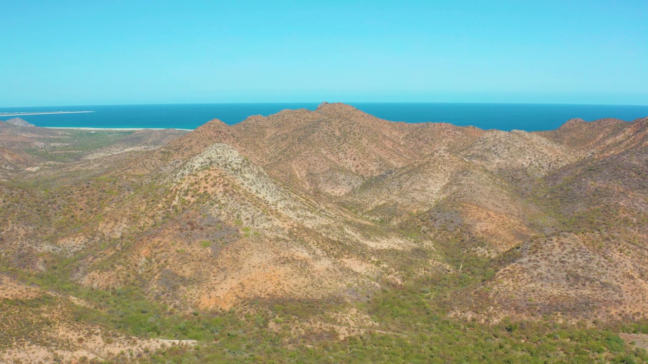 Rocky coastal mountains under clear sky with ocean beyond.