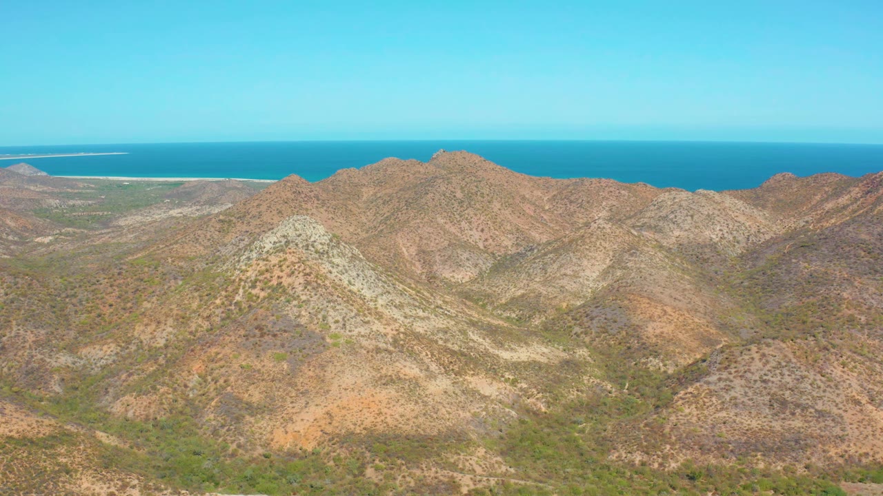 Cabo Pulmo aerial view with a pale rocky ridge near center, brown hills across the frame, blue water behind them, and no visible people.