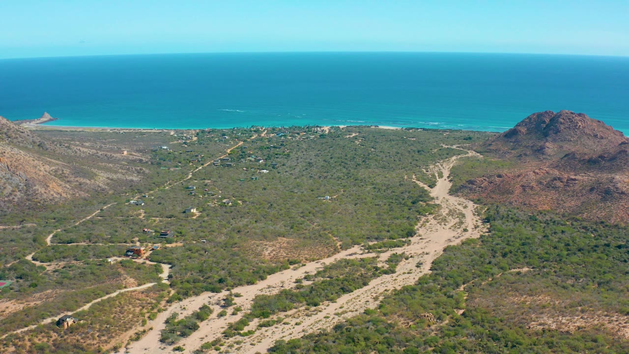 Aerial coastline with green scrub, sandy washes, and ocean horizon.