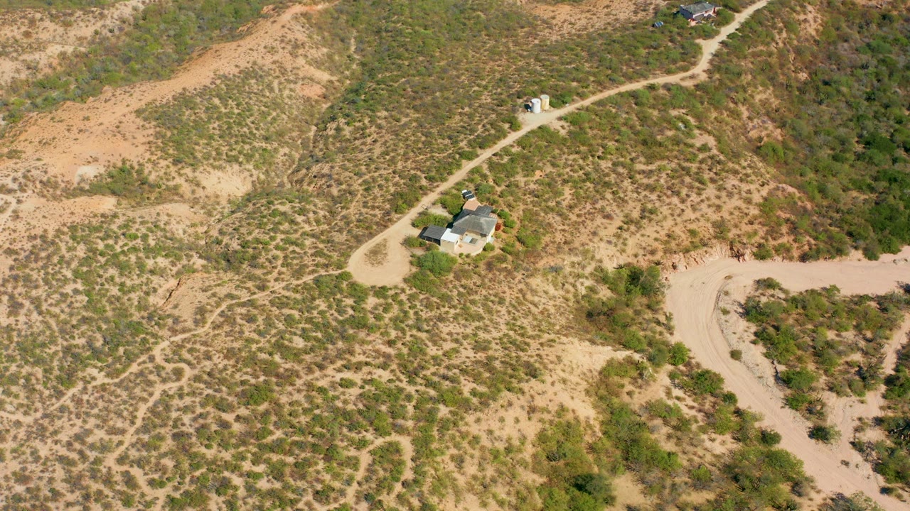 High aerial view in Cabo Pulmo, Baja California Sur showing a small house near winding pale dirt roads across dry scrub hills, with no visible people.