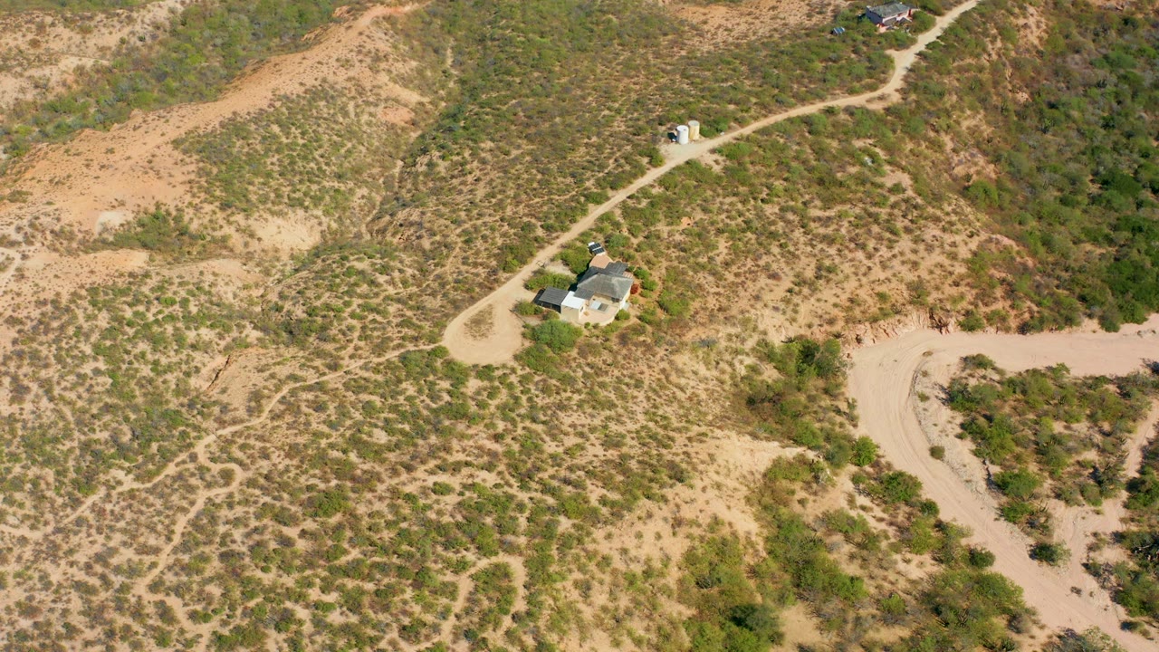 Aerial frame in Cabo Pulmo, Baja California Sur with the small house slightly left of center, pale dirt roads curving through scrub-covered sandy terrain, and no visible people.