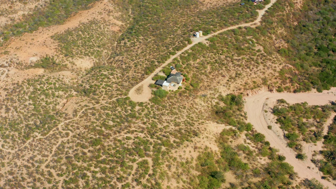 High oblique view of a rural house and branching dirt roads on arid hills.