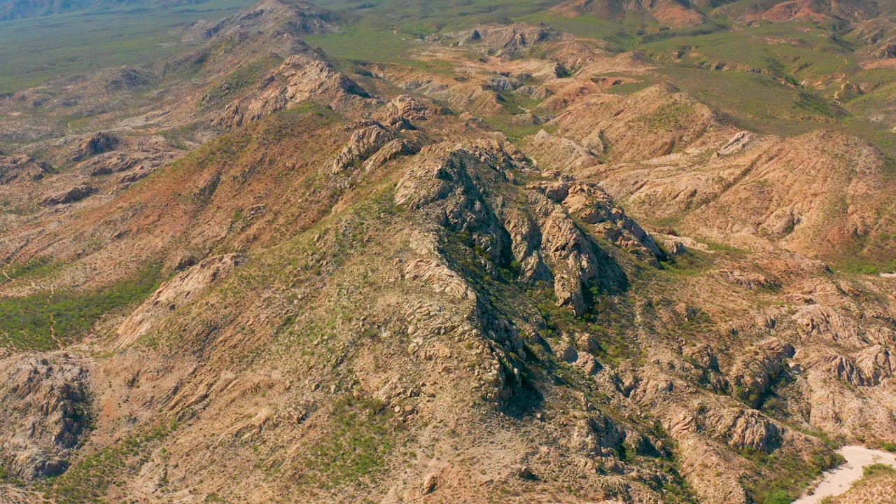 Cabo Pulmo aerial view looking across a central rocky ridge, tan valley floor, scattered green patches, and no visible people.