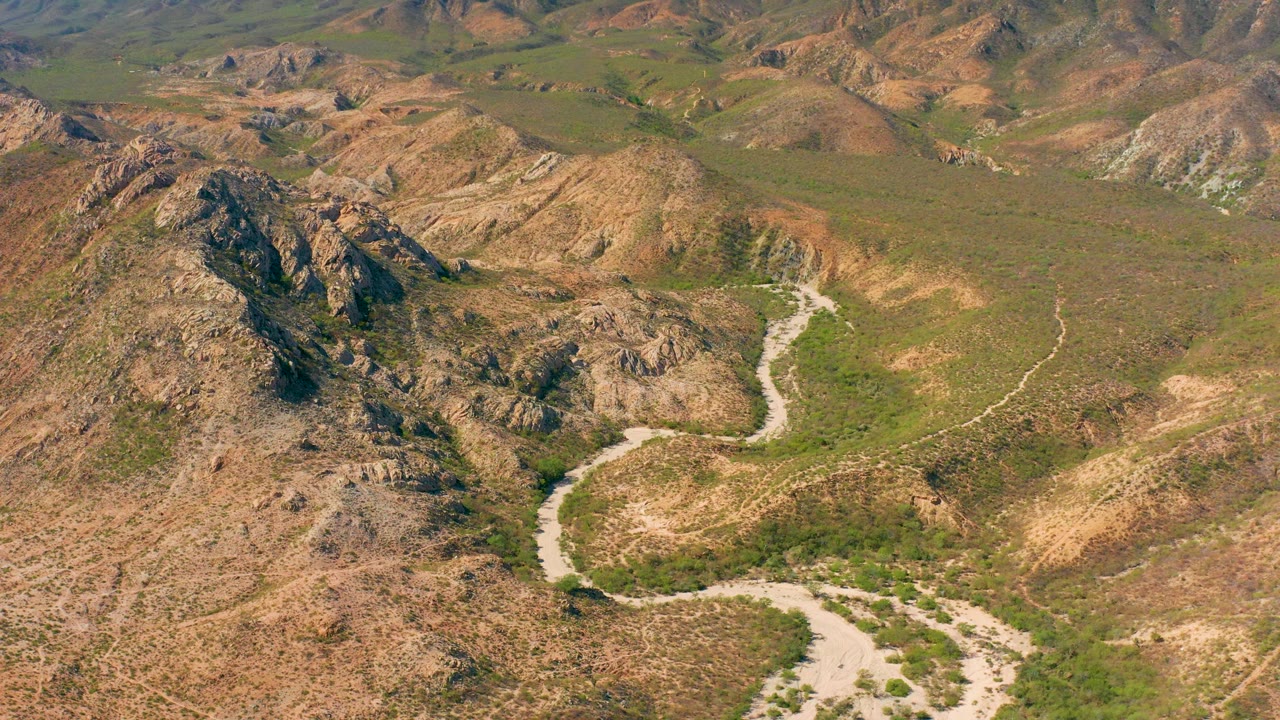 Aerial road curve below jagged hills and scrubland.