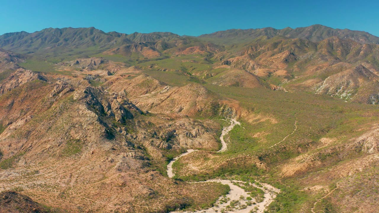 Wide aerial view of a mountain valley with rocky hills and blue sky.